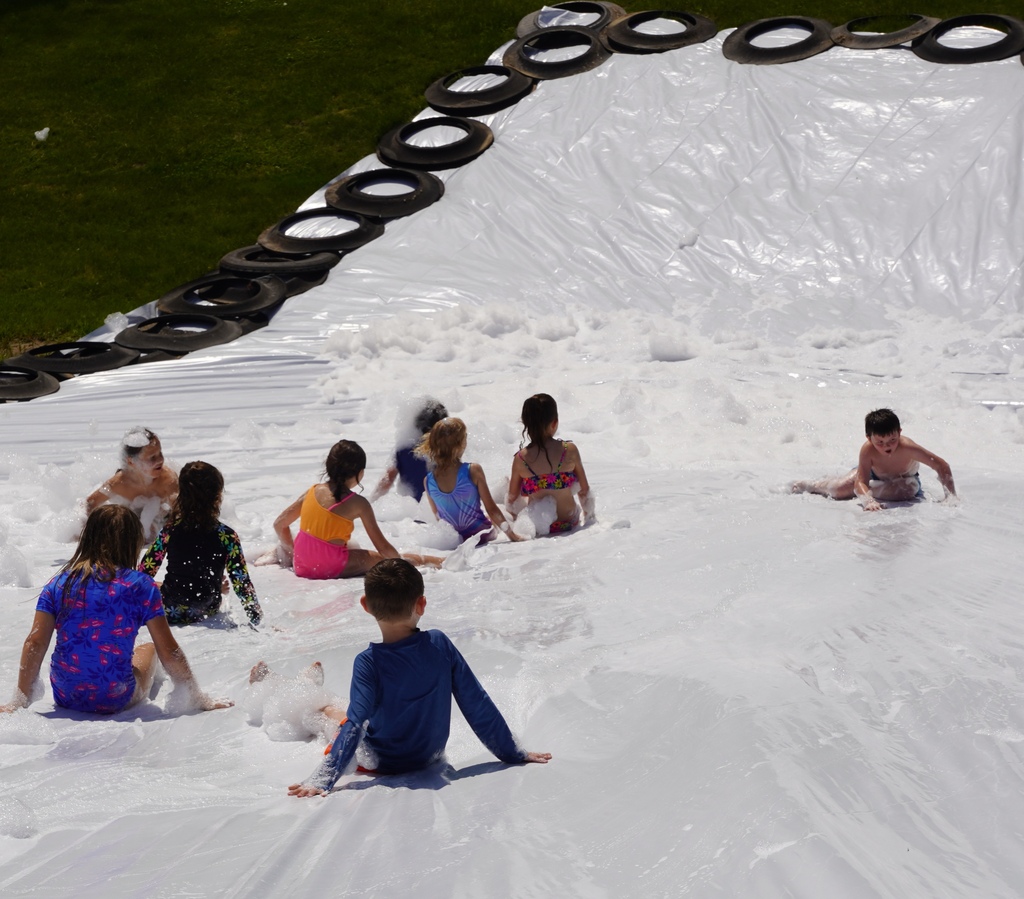 Kids play in foam and slide down a large tarp that is placed over a hill