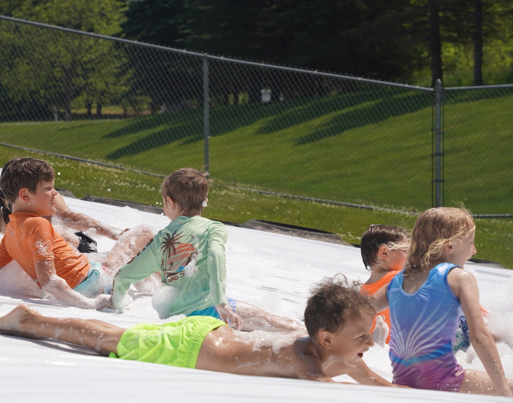Kids play in foam and slide down a large tarp that is placed over a hill