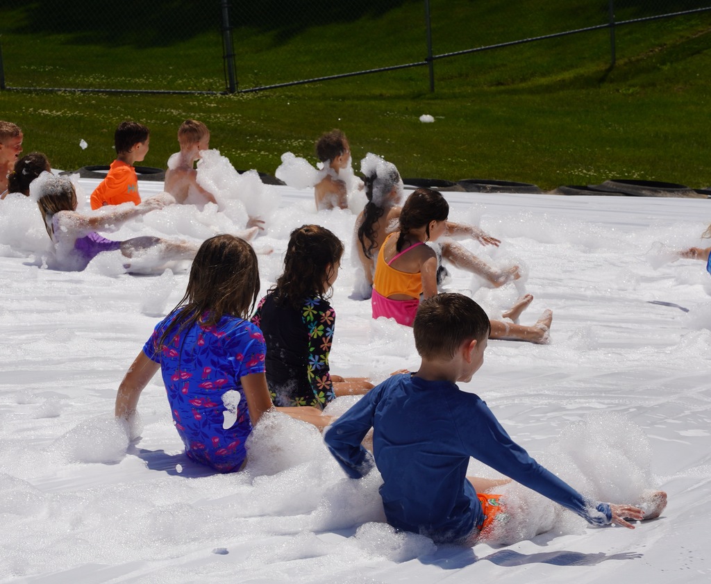 Kids play in foam and slide down a large tarp that is placed over a hill