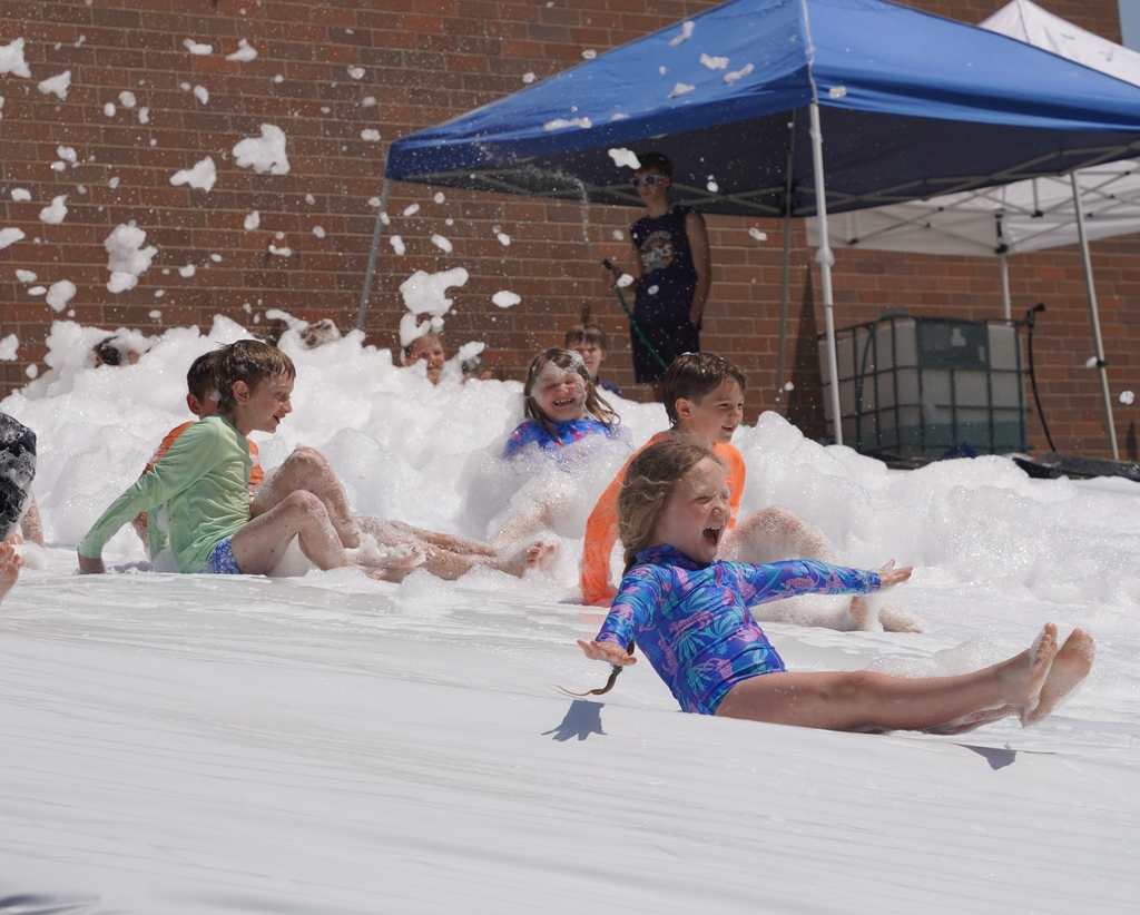 Kids play in foam and slide down a large tarp that is placed over a hill