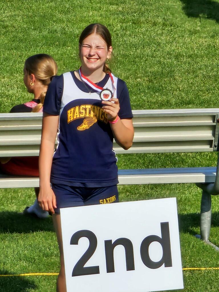 A female athlete holding up a medal with a sign that says 2nd in front of her.