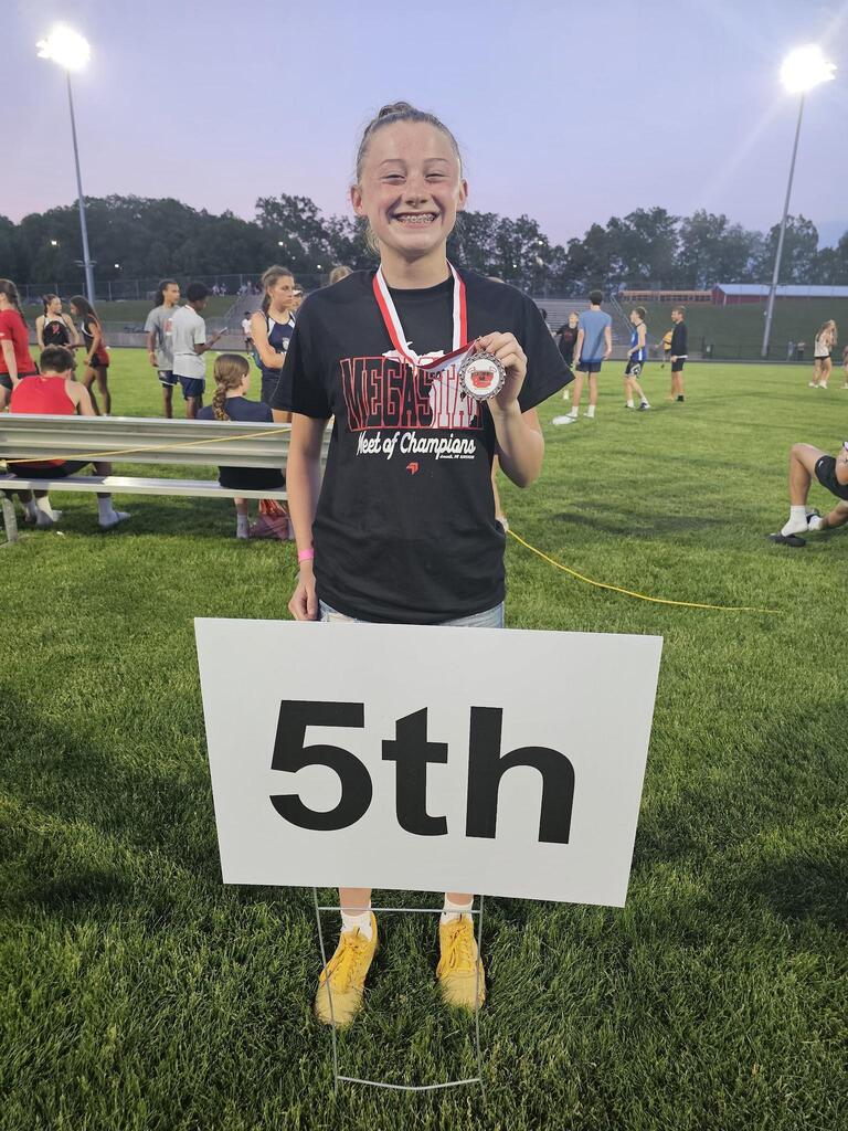 A female athlete holding up a medal with a sign that says 5th in front of her.