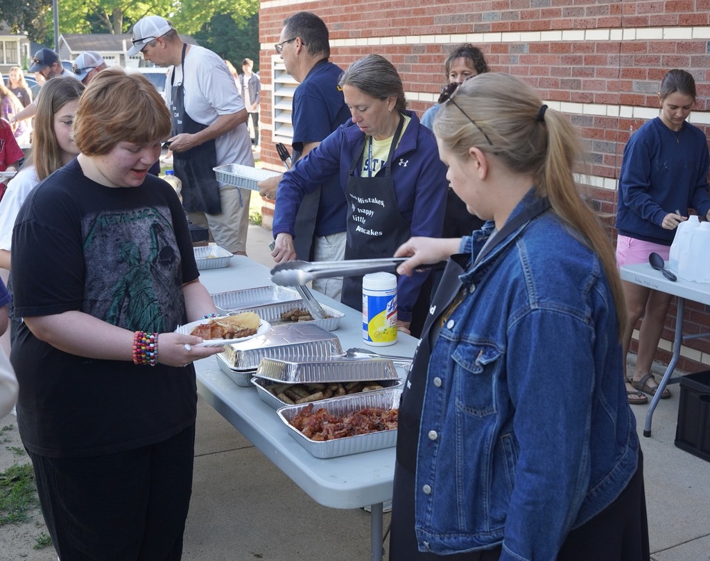 Teachers handing out plates of breakfast food to a long line of students