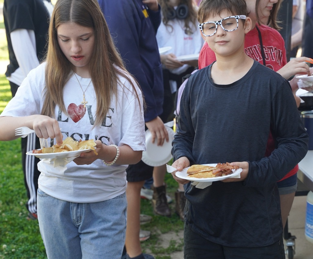 Teachers handing out plates of breakfast food to a long line of students