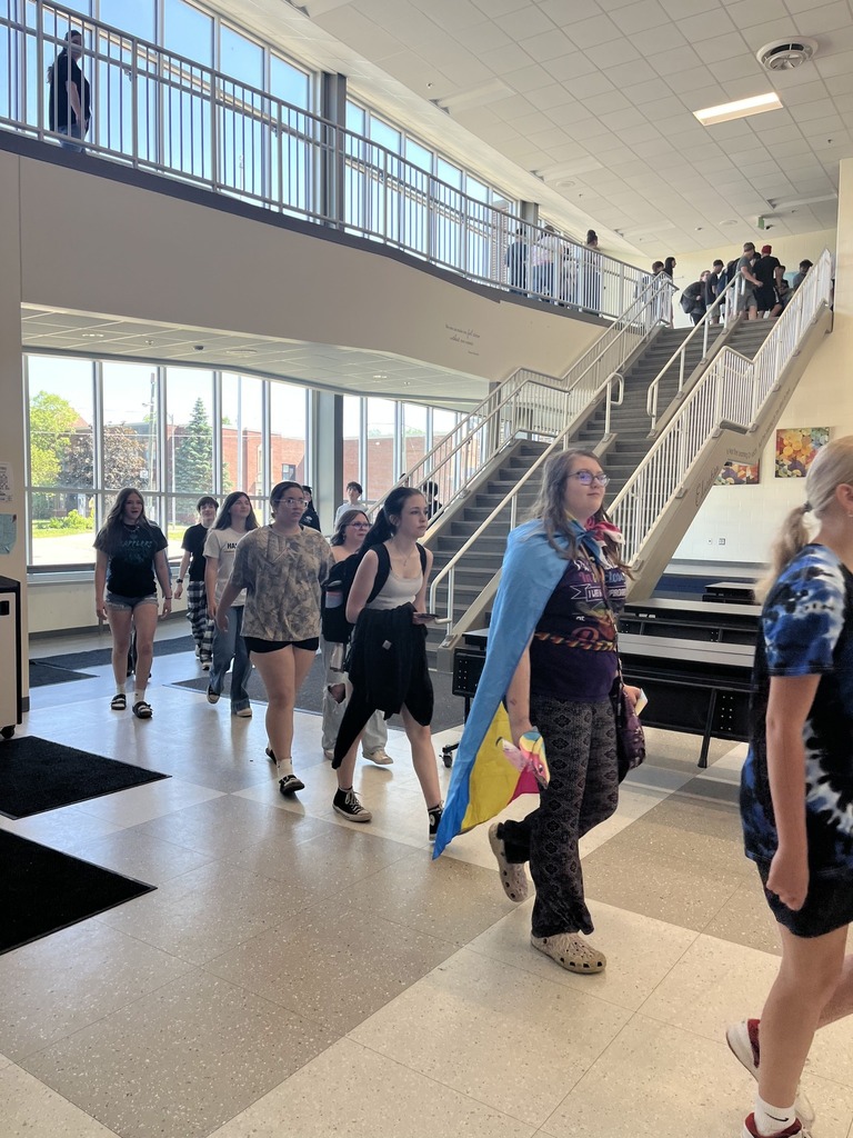 Students walk in a single file line through a open room of school.