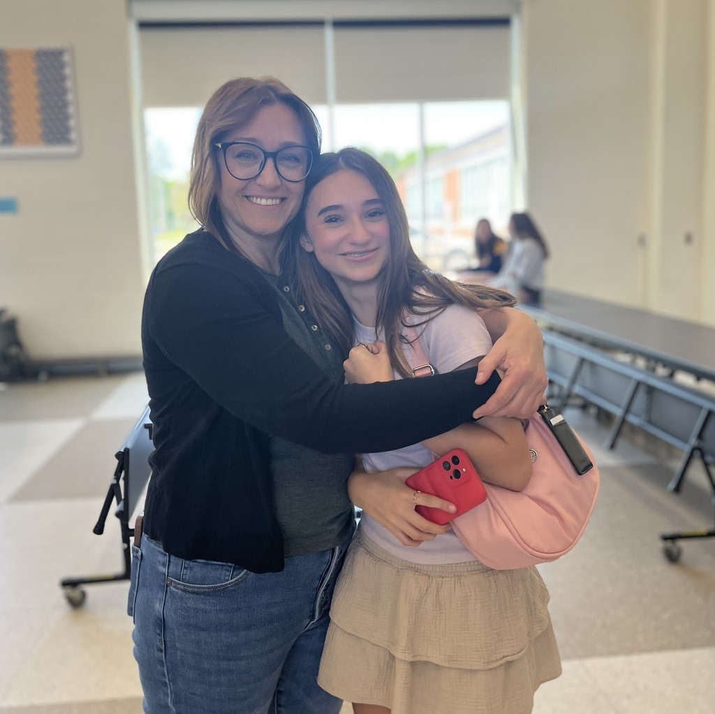 A woman and young female student embrace and pose for the camera
