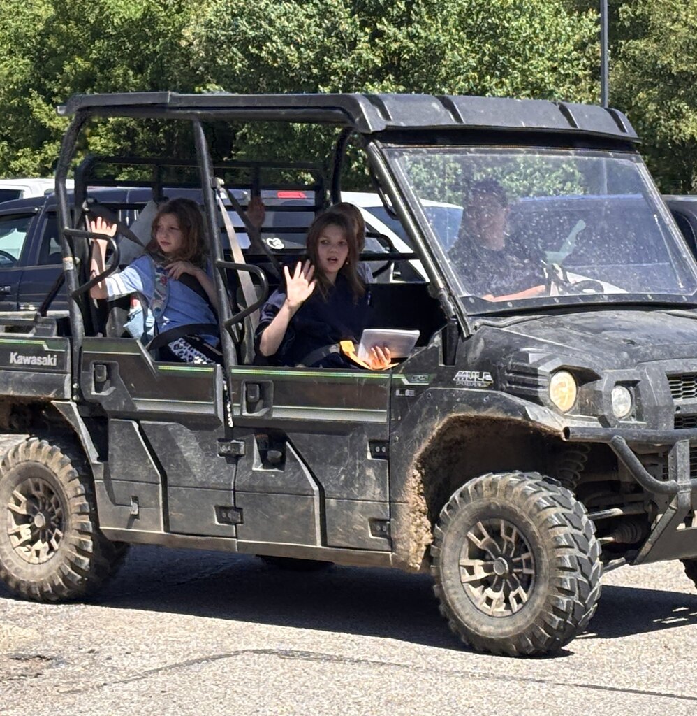 Young students seated in a side-by-side vehicle wave goodbye