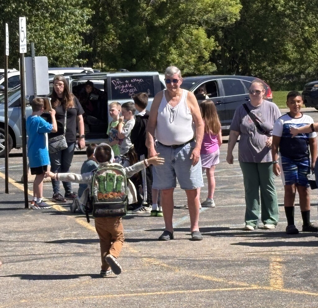 A student with a backpack on run towards an adult with his arms open for a hug
