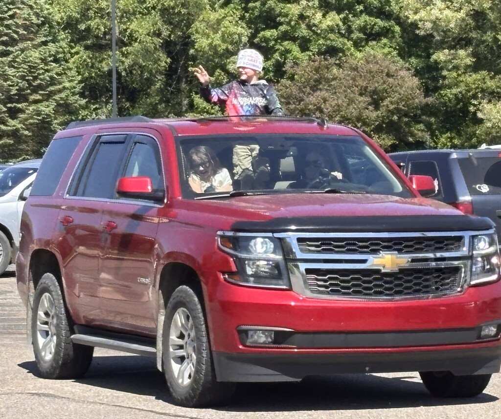 A student sticks his head out of the sun roof of a vehicle and waves goodbye