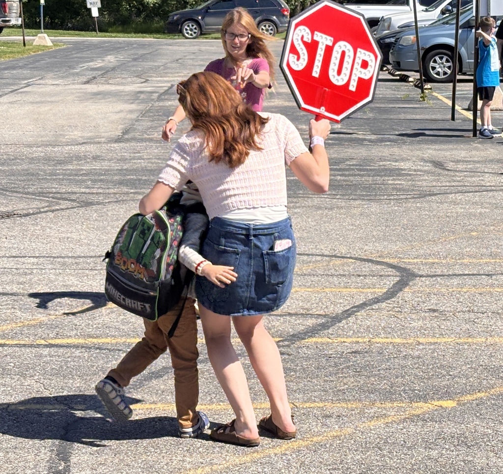 A child runs up to a crossing guard holding a stop sign and gives her a hug