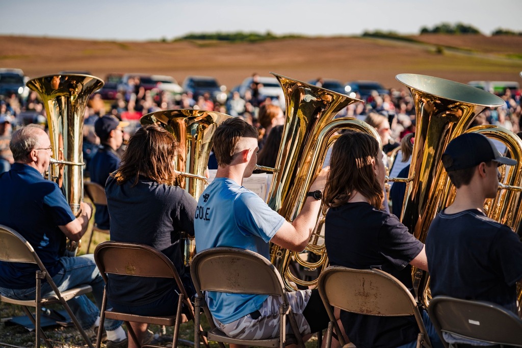 A grroup of Tuba players are seated and performing
