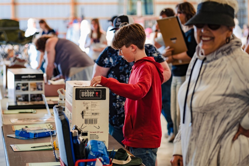 In a crowded barn of people, a boy inspects prizes that are displayed on a table