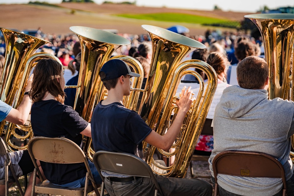 The rear view of a line of seated tuba players playing their instruments