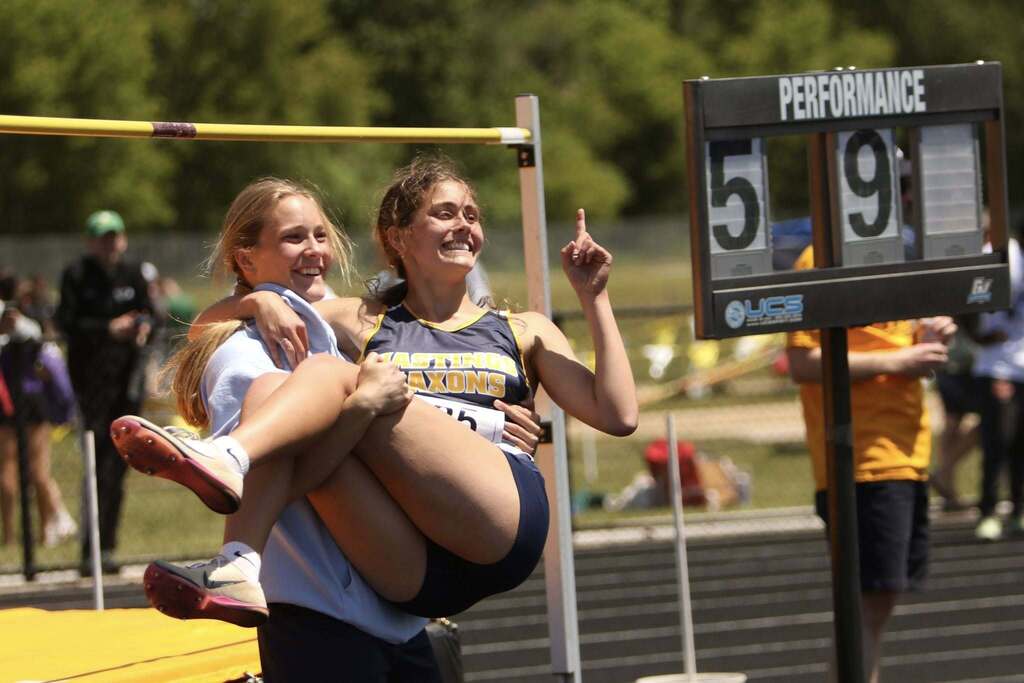 One girl holds another like a baby. The one being held holds up a #1 fingr