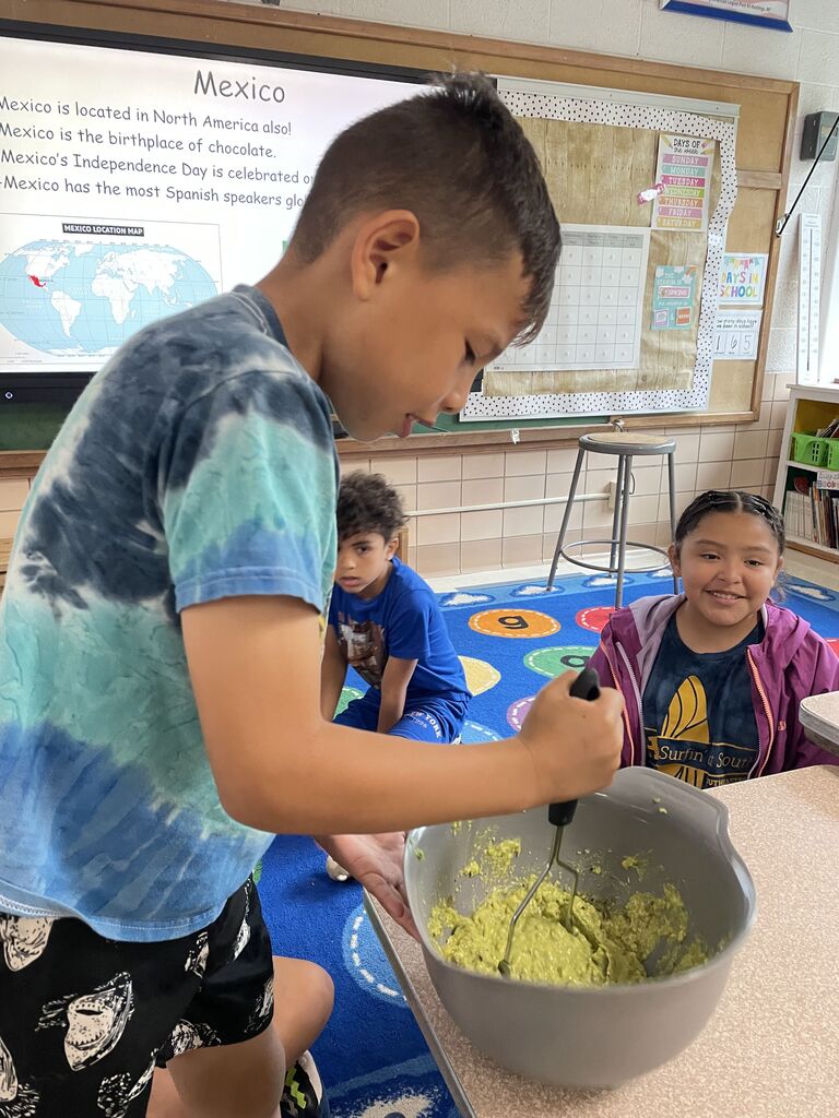 A boy is standing and crushing up a green substance in a mixing bowl