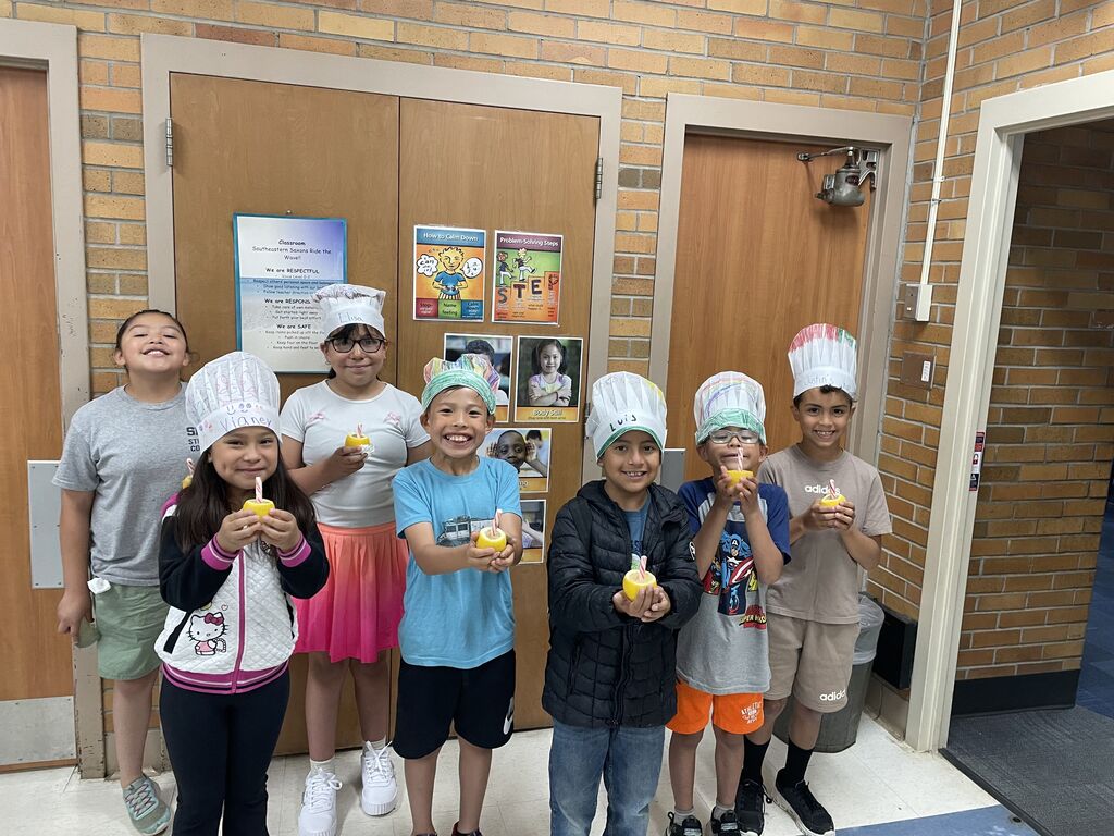 A group of students wear makeshift chef hats and hold up an edible creation