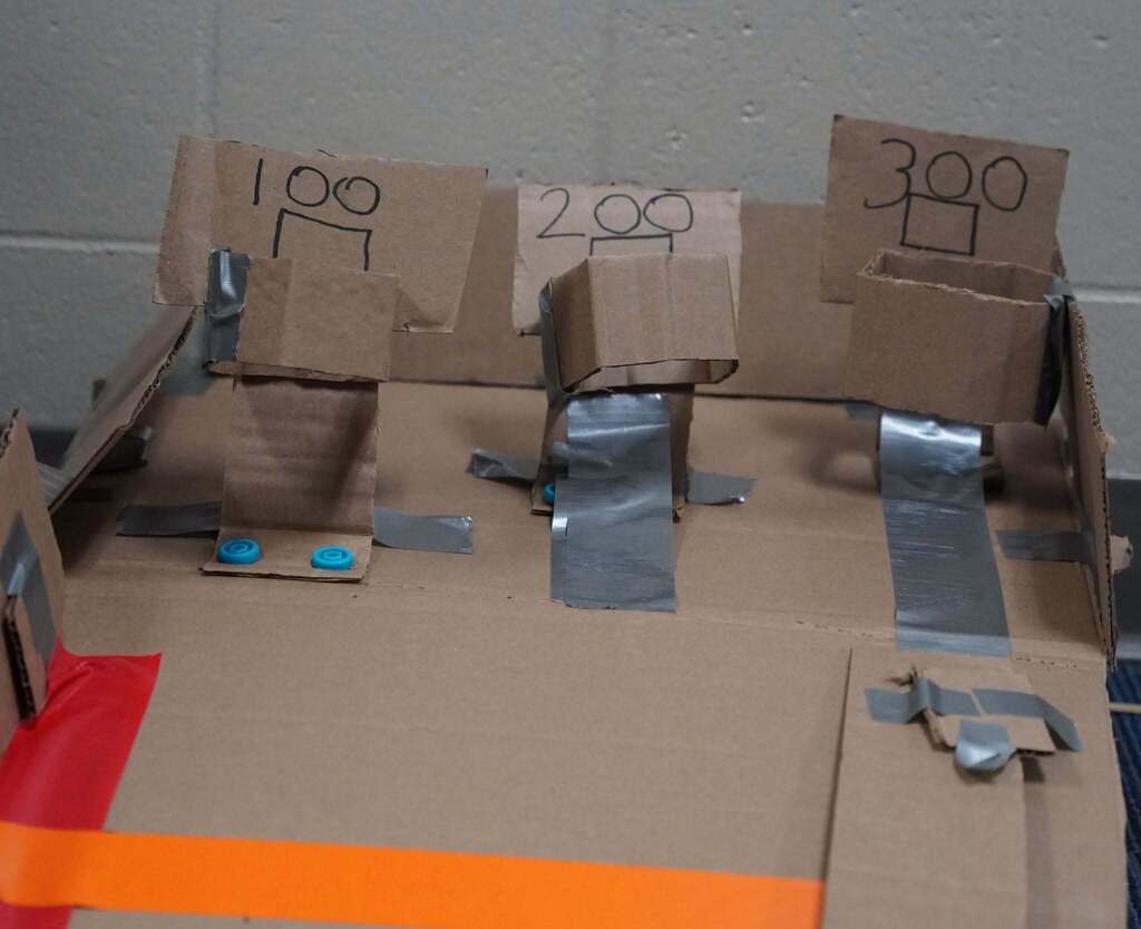 A close up of a hand-made cardboard game. Three basketball hoops were created numbered with 100, 200 and 300