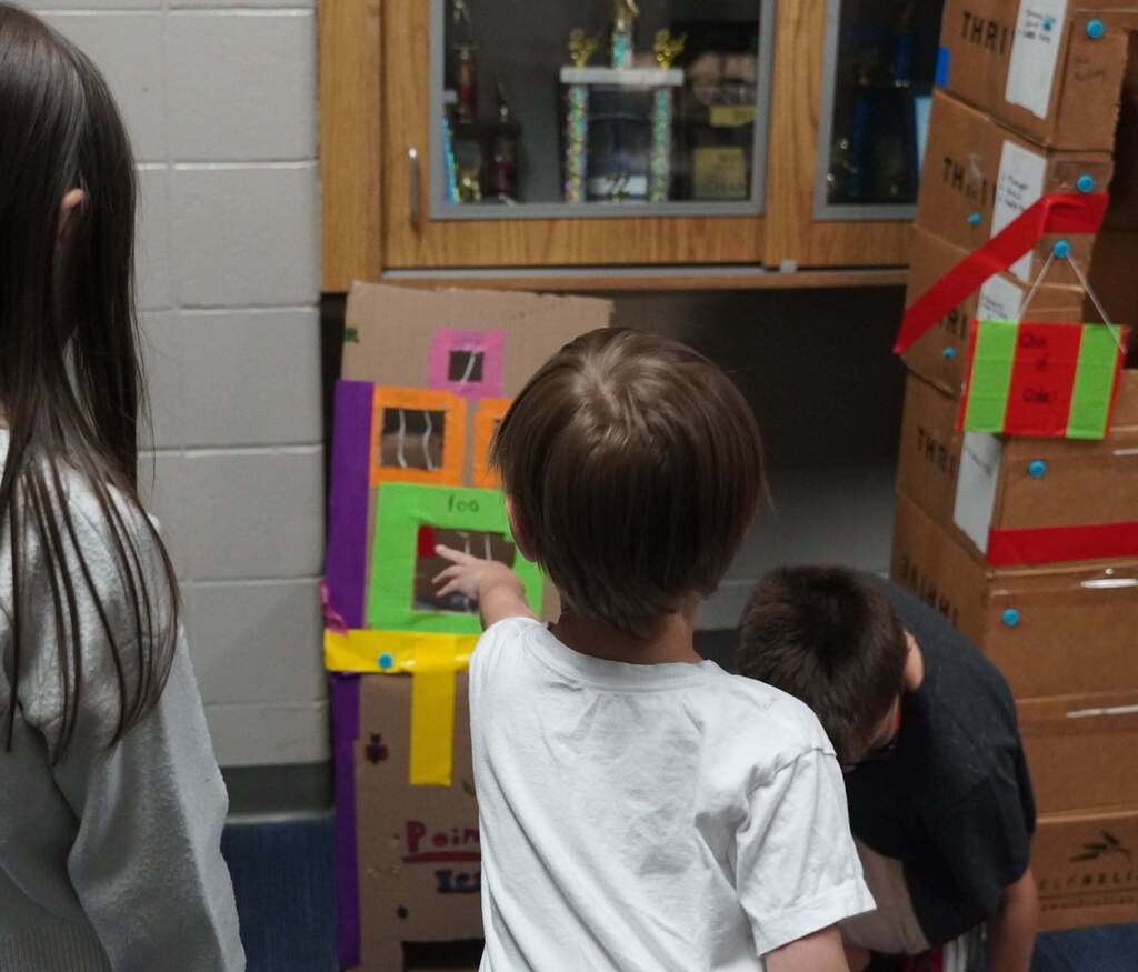 A child tosses a projectile at a piece of cardboard with several openings in it as part of a game.
