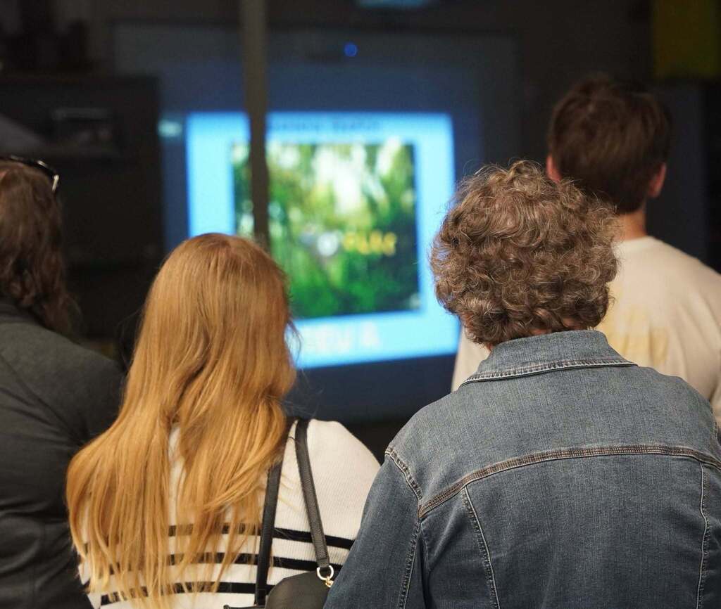 The photo shows the back of heads of some parents who are watching a screen that features stop-motion videos made by students.