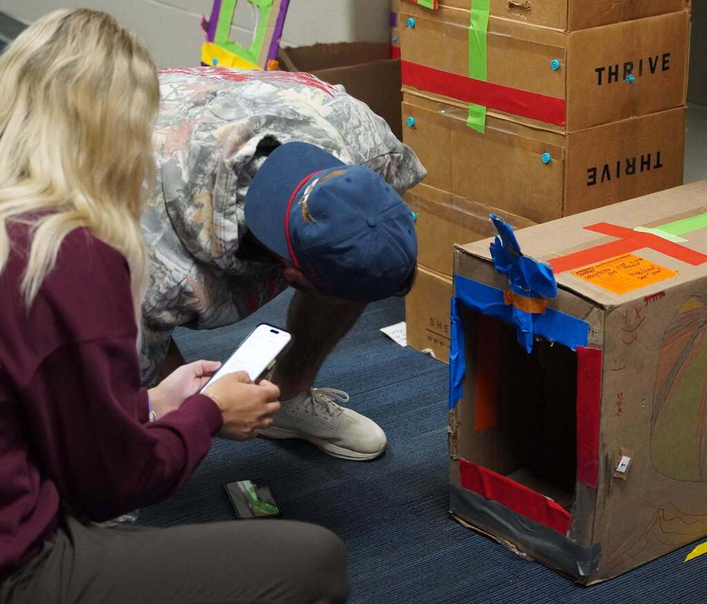 A man bends down to look inside a cardboard box that has been fashioned into a game.