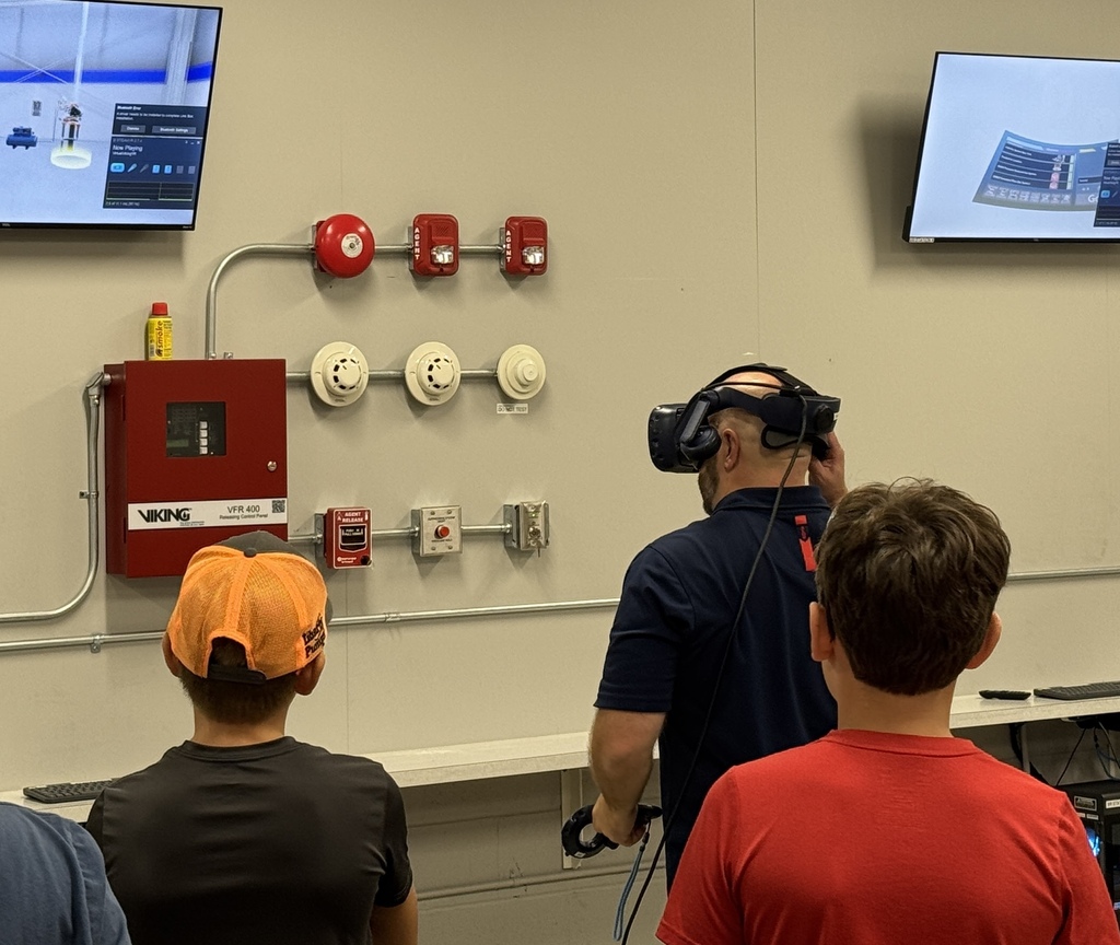 A man is wearing virtual reality goggles while two boys look on.