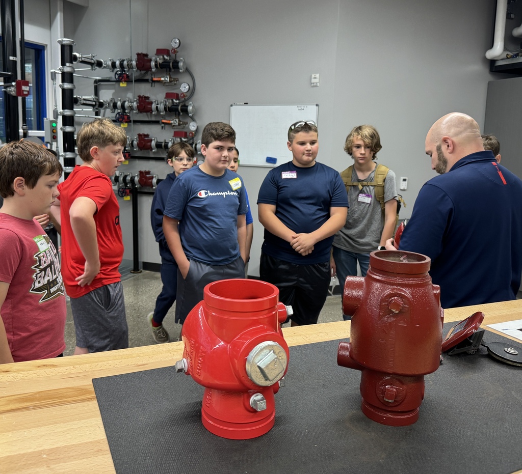 A number of students face a table where large, metal objects are setting.