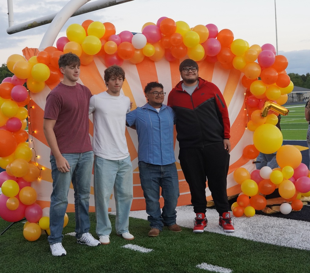 Four male students pose for a picture with a colorful background, which includes balloons, behind them.