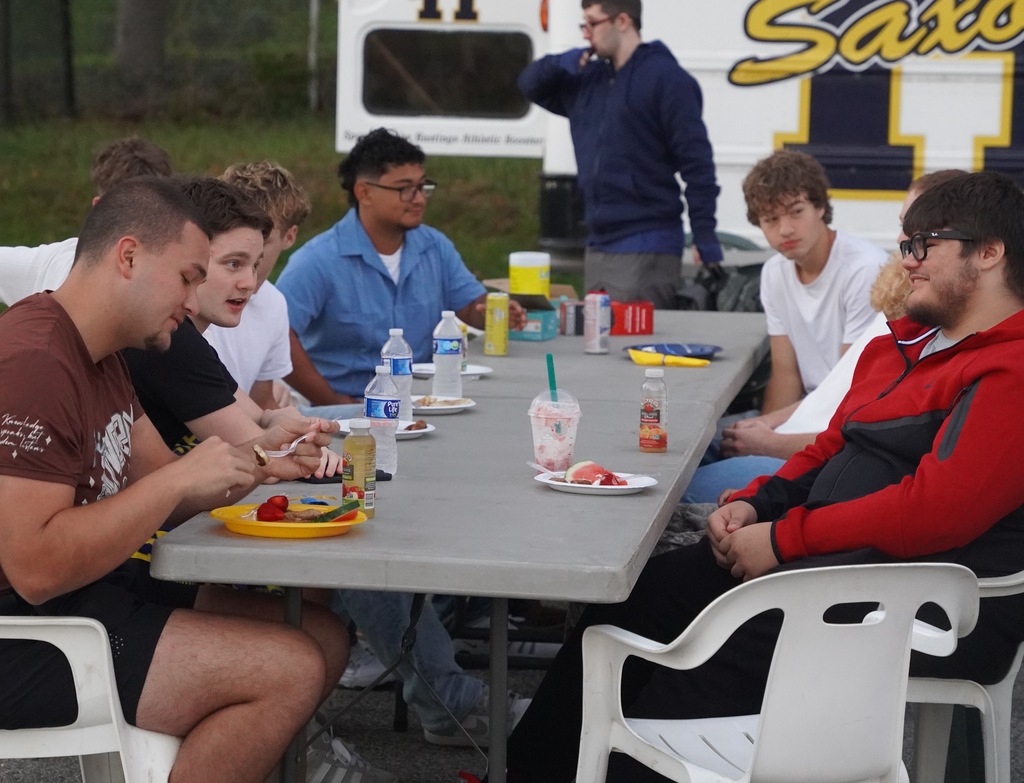 Students are seated on both sides of a long table eating breakfast and talking to each other.