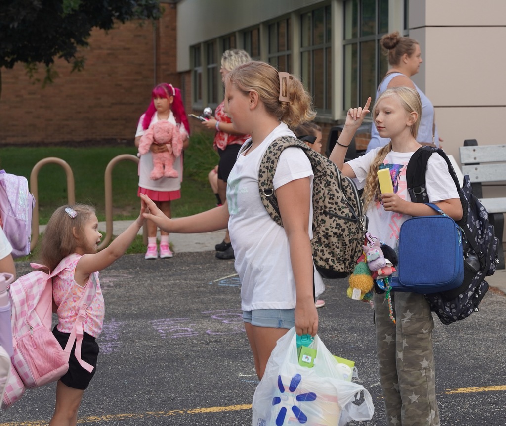 An older female student with a backpack gives a high five to a smaller girl.