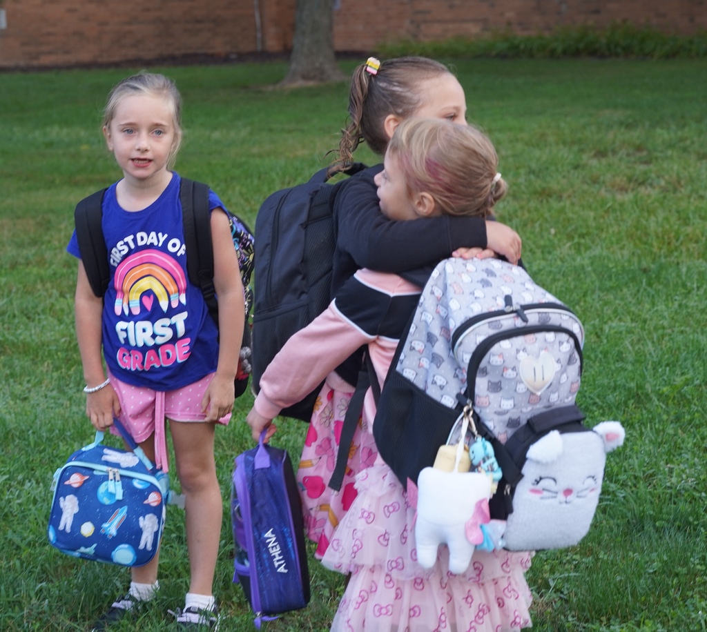 Two femaile students exchange a hug with another girl looking on