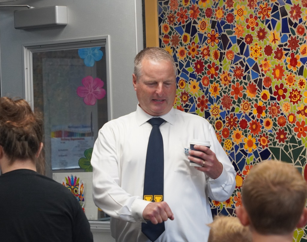 A man with a tie stands at the door to a school giving fist bumps to students who enter.