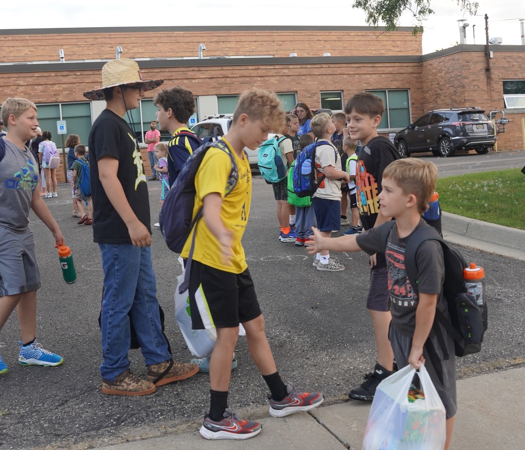 Two students with backpacks on their back exchange a high-five