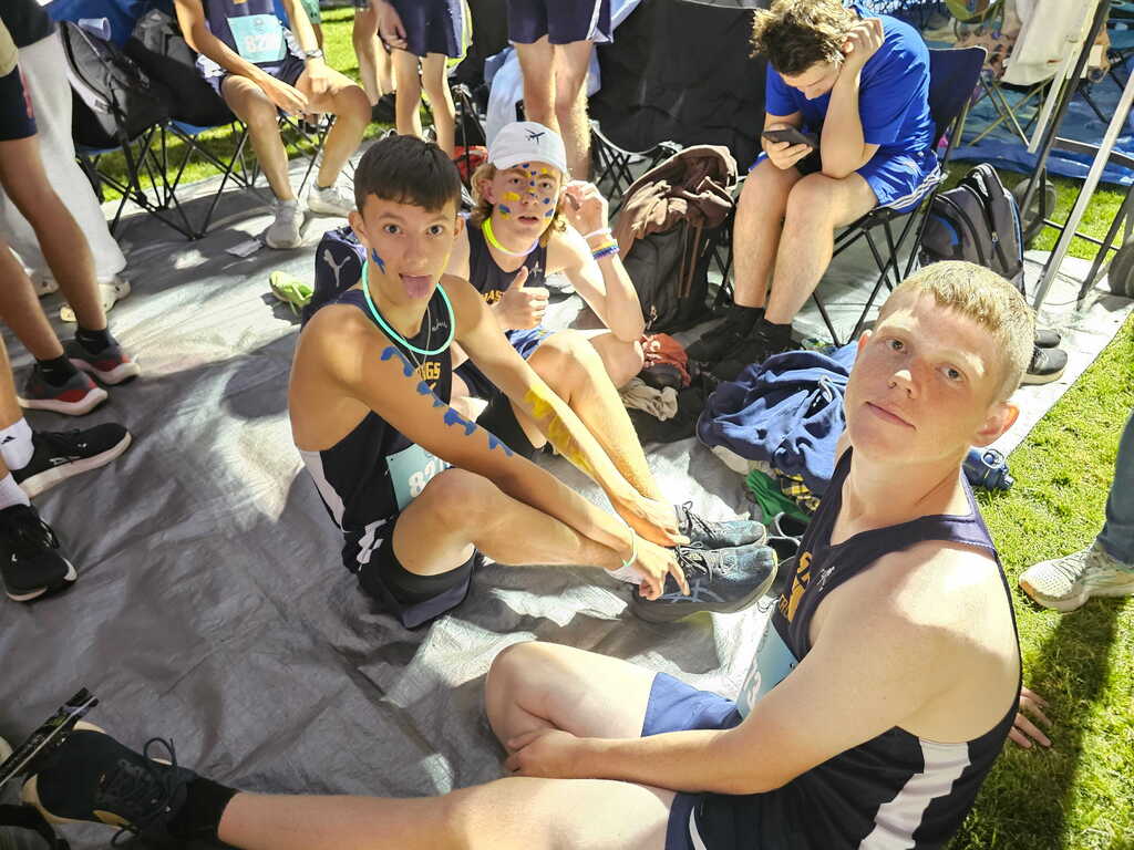 three boys in navy blue uniforms sit on the ground looking at the camera. two of them have glow sticks around their necks like a necklace.