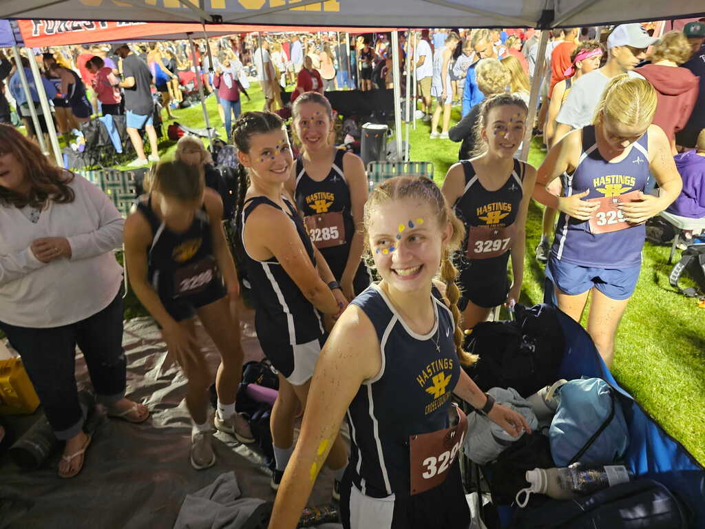 A group of female students with navy blue tank tops on smile for the camera.