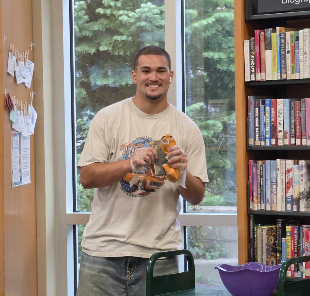 A male student stands, flanked by book shelves, smiling at the camera.