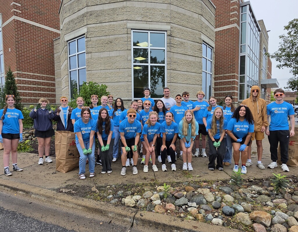 A large group of student, all in uniform blue shirts, pose for a group photo in front of a large stone building.