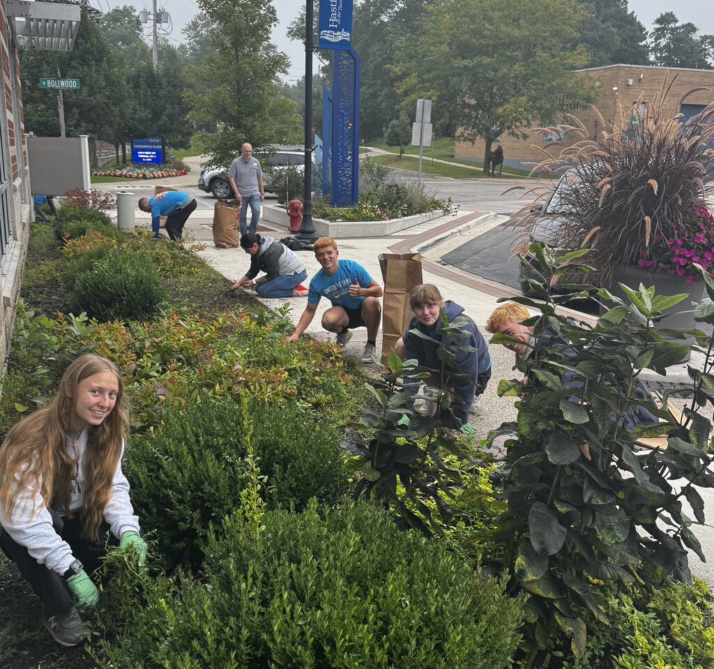 A number of students all in uniform blue shirts work on pulling weeds from a section of landscape.