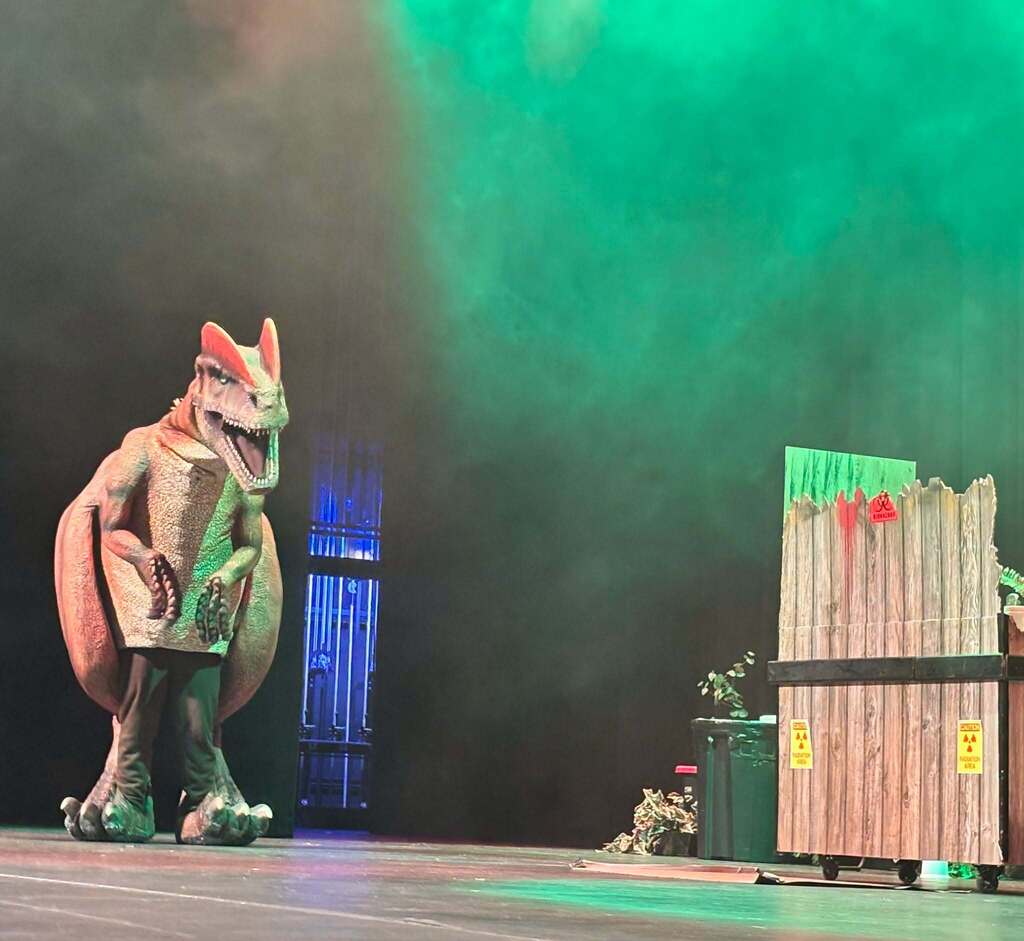 A large dinosaur walks on to a stage with fog hovering in the air.