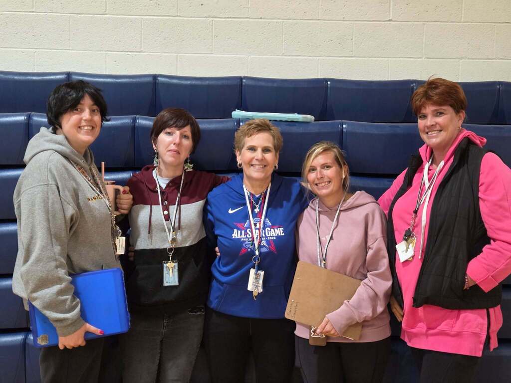 Five women dressed alike with short hair and sweatshirts posing for the camera.