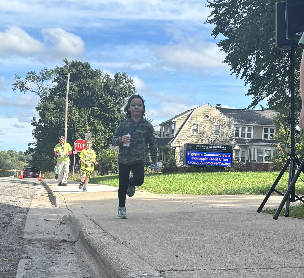 A young girl runs down the sidewalk toward the camera with a smile on her face.