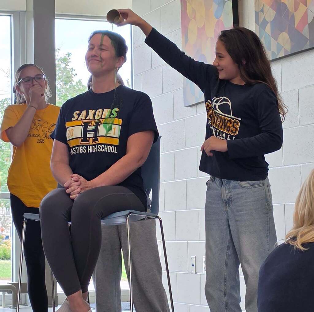A woman sits in a chair smiling as girl dumps slime on her head. Another girl is in the background chuckling