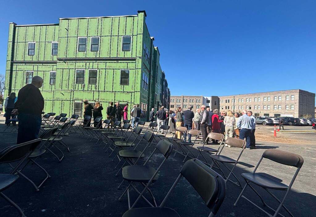 A grroup of people gather around, talking with buildings that are under construction in the background.