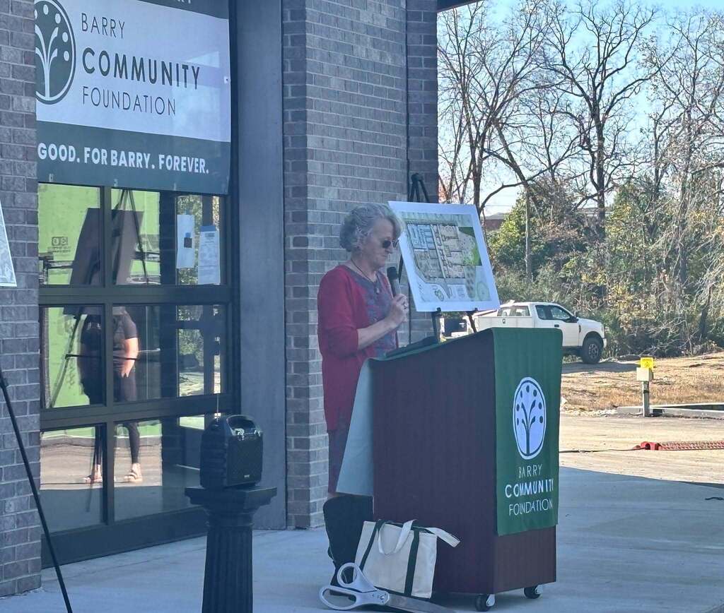 A woman stands at a podium with a microphone to her mouth speaking.