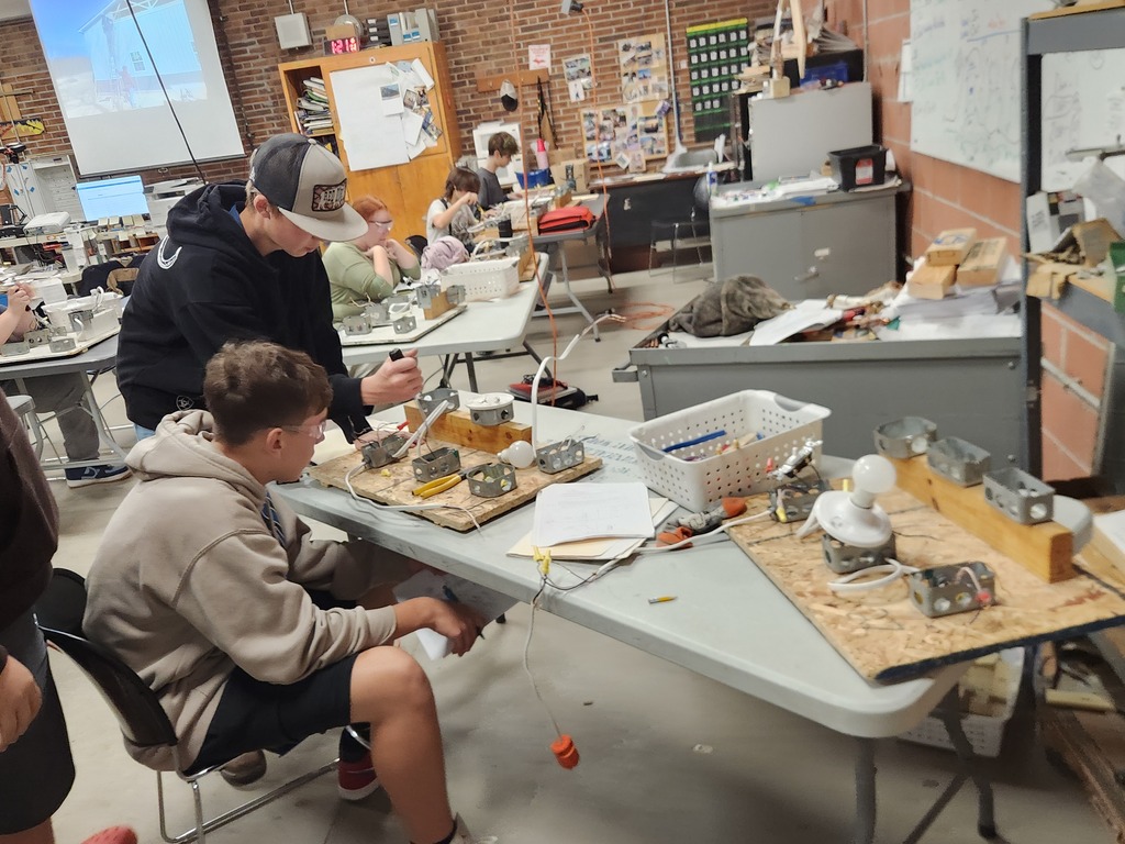 Two male students sit at a table and  examine planks of wood and metal brackets.