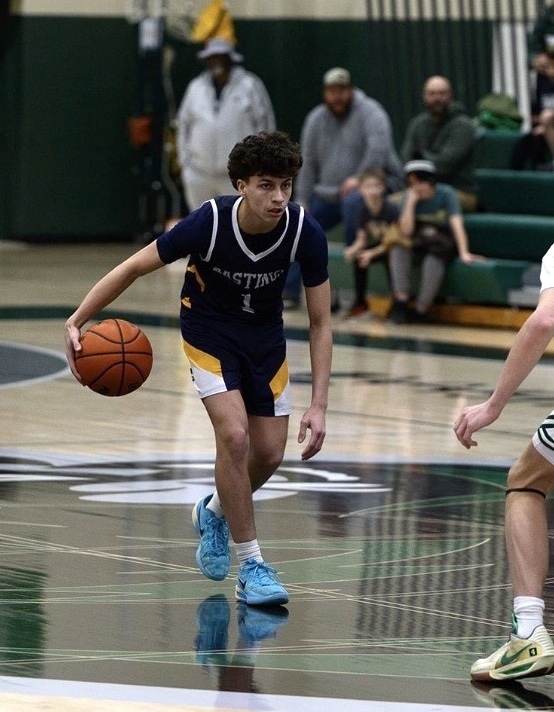 Male high school student on a basketball court with a blue jersey on dribbling the ball.