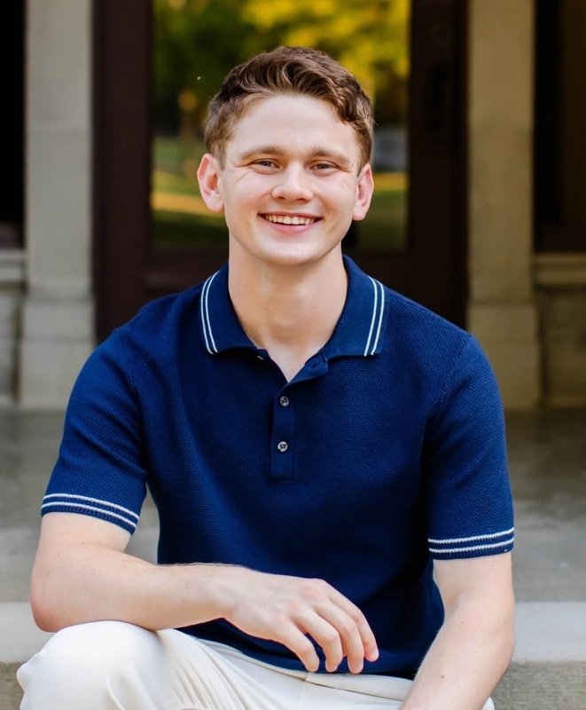 A male high school student with a dark blue shirt on facing the camera and smiling