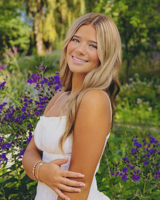 A female high school student wearing a white dress and smiling at the camera.