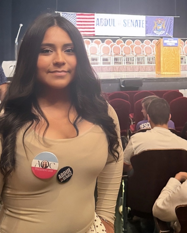 A female high school student who is wearing a tan shirt with political pins fastened to it.