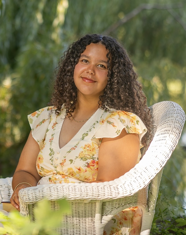 A female high school student seated in a white wicker chair facing the camera and smiling.