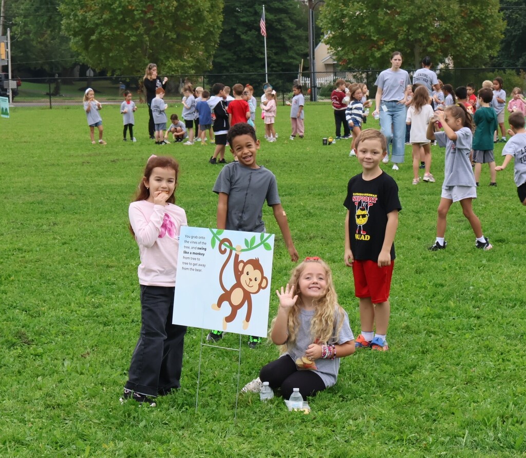 Students smile and wave from the grass.